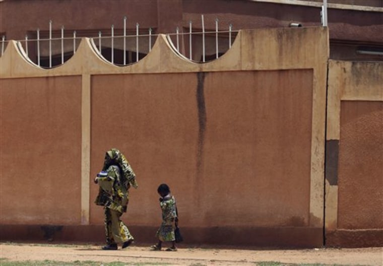 A woman and child walk past the fence surrounding the compound of the Libyan embassy in Niamey, Niger, on Monday. A convoy carrying ousted Libyan leader Moammar Gadhafi's son al-Saadi has crossed into neighboring Niger, a spokesman for Niger's government said on Sunday.